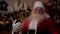 Shocked Santa Claus looks at smartphone, turns head in surprise, looks camera