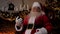 Shocked Santa Claus looks at smartphone, turns head in surprise looks camera