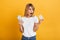 Shocked surprised young blonde woman posing isolated over yellow wall background dressed in white casual t-shirt using mobile