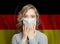 Shocked woman in medical mask on German flag background. Flu epidemic and domestic violence in Germany concept