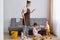 Shocked woman wearing white t shirt, brown apron and jeans, cleaning house, posing with her daughters, washing floor, upset that