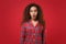 Shocked young african american girl in pajamas homewear posing while resting at home isolated on red background in