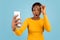 Shocked young black female in yellow t-shirt takes off glasses and looks at smartphone reads amazing message