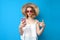 Shocked young girl in a sun hat and glasses holds a smartphone and is surprised on a blue isolated background, a woman points to