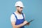 Shocked young man in coveralls protective helmet hardhat hold clipboard with papers document isolated on blue background