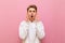 Shocked young man standing on a pink background, looking mad at the camera and putting his hands to his face. Portrait of