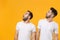 Shocked young men guys friends in white blank empty t-shirts posing isolated on yellow orange background in studio