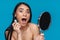 Shocked young woman apply lash mascara holding mirror