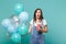 Shocked young woman keeping mouth open, hold plastic cup of cola or soda, celebrating with colorful air balloons