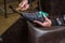 Shoemaker in leather apron making shoes in workshop. Male hands holding suede gray shoe on last and hammer. Closeup