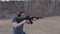 The shooter makes a series of shots from a black assault rifle on the shooting range. Side view. The camera is in motion.