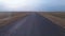 Shooting a drone quickly flying over deserted road in the middle of agricultural fields with harvested crops in village