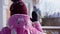 Shooting over shoulder of teen girl waving in slow motion to blurred senior woman standing on porch on winter day