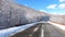 Shooting windshield of car, by road winding between wooded snow covered hills