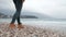 Shooting woman legs walking on sea shore close to blue water.