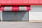 Shop retail with metal shutters closed and a red white awning. Sidewalk and asphalt road in front.