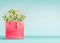 Shopping bag in living coral color with flowers bunch standing on table at turquoise wall background. Branding mock up. Copy space