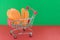 Shopping basket on a red and green background with plastic chicken and sausages inside. The concept of unnatural products with