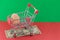 A shopping basket on a red and green background with a plastic egg stands on a banknote. The concept of unnatural products with