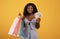 Shopping budget. Millennial African American woman holding money and bright shopper bags over orange background