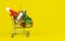 Shopping cart with christmas tree and miniature gift boxes on yellow background. Christmas and New Year shopping time background