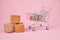 Shopping cart with package boxes on pink background. Shopping and delivering concept. Shop trolley full of parcels