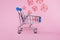 shopping cart with red percentage signs on cubes on pink background, retail and discount concept