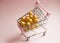 Shopping cart. Supermarket trolley full of golden balls on pink background. Consumerism concept photo.