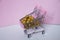 Shopping cart. Supermarket trolley full of golden balls on pink background. Consumerism concept photo.