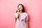 Shopping. Cute candid woman smiling, showing plastic credit card on face, standing in dress against pink background