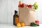 Shopping paper bag with different groceries on table against white wooden background