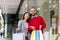 Shopping time. Young multiracial couple holding bright shopper bags, smiling at camera near city mall