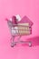 Shopping trolley full of wrapped gifts on pink background