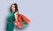 Shopping woman. Girl in green dress, holding bags, grey background. Copy space for some text. Consumerism, rebates, sales ad