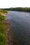 The shore of a calm river with stony banks overgrown with grass