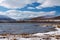 At the shore of mountain lake in windy weather with yellow grass covered with snow in September