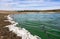 Shore of the ValdecaÃ±as reservoir with green pollution in the water and a white foam on the shore