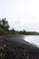 The shoreline of the black sand and pebble beach of Hana Bay lined with rain forest and the Pacific Ocean in Hana, Maui