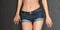 Short blue Jean shorts on the body of a young tanned girl on gray background