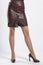 short brown leather skirt with a leather belt close-up, women`s feet with black high-heeled shoes on a white background