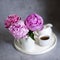 Short cropped bouquet of fresh peonies in porcelain jugs on a white tray on a gray craft background