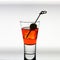 Short drink glass with red liquid, olive, ice cubes