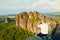 Short hair man on cliff of rock and takes photo by smart phone of landscape bellow. Sunny day in rocky mountains