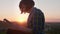 short-haired brunette woman with digital tablet sits on mountain rock at sunset