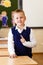 Short-haired eight-year-old handsome schoolboy stands in class in school uniform