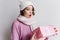 Short-haired european girl in hat posing emotionally, looking at new year present. Indoor photo of amazed young lady in