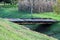 Short homemade wooden bridge with strong metal beams support connecting two sides of small canal behind local gardens with trees