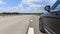 A short stop during a summer road trip. The car is parked on the side of an asphalt highway with markings and a dividing fence. Mi