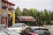 A shot of the Angry Crab Shack surrounded by lush green trees with tall black light posts with cars driving on the street