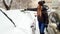 Shot of blond smiling girl in jacket clean up the snow covered car . Scraping the windshield of snow at the early snowy